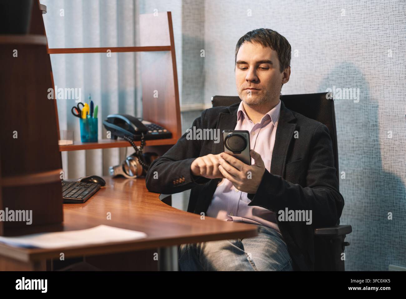 Uomo d'affari che scorre notizie o social media sul suo smartphone mentre riposa con i piedi sollevati. Rilassamento in ufficio e svago digitale. Foto Stock