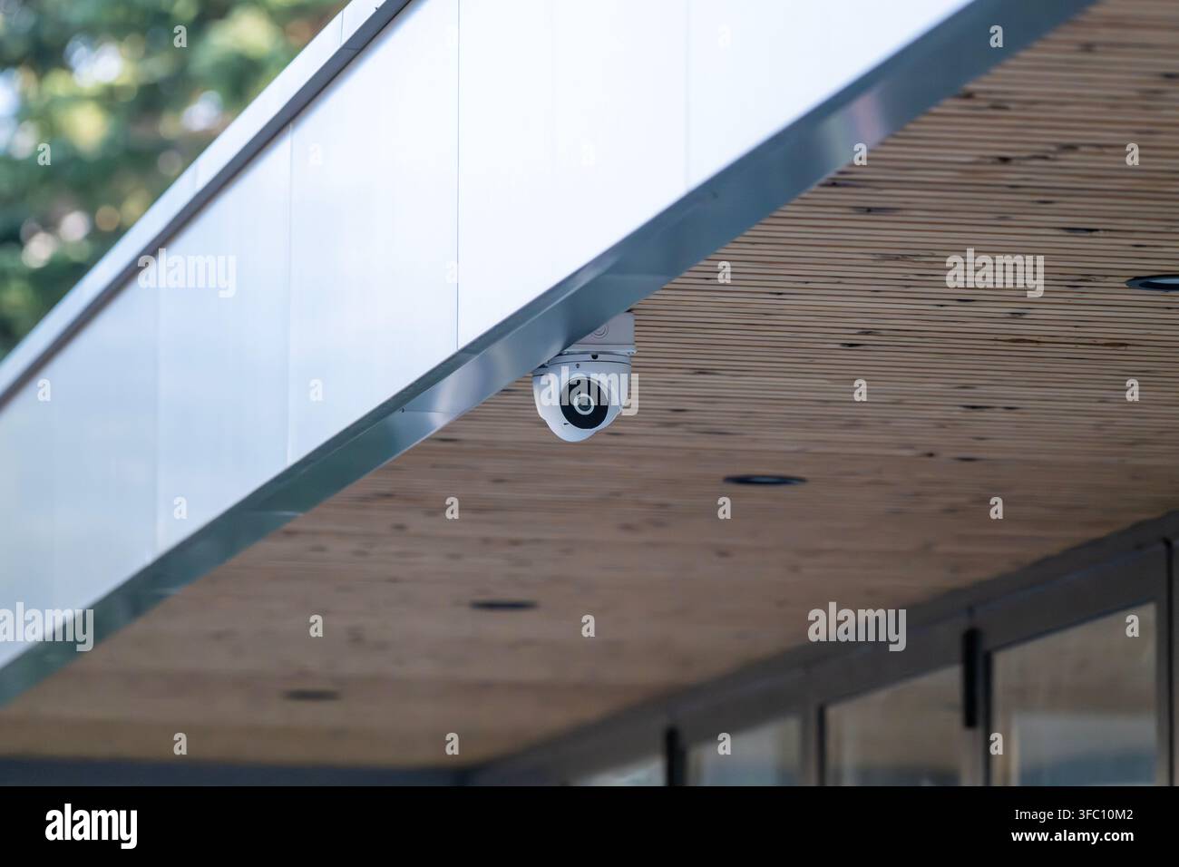 Una telecamera di sicurezza moderna è montata sotto la sporgenza in legno del tetto dell'esterno di un edificio. Foto Stock