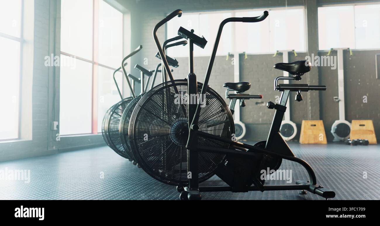 Vuoto, fitness e airbike in palestra per cardio, struttura benessere e setup per la classe spin con stile. Bicicletta stazionaria, interno e attrezzature in Foto Stock