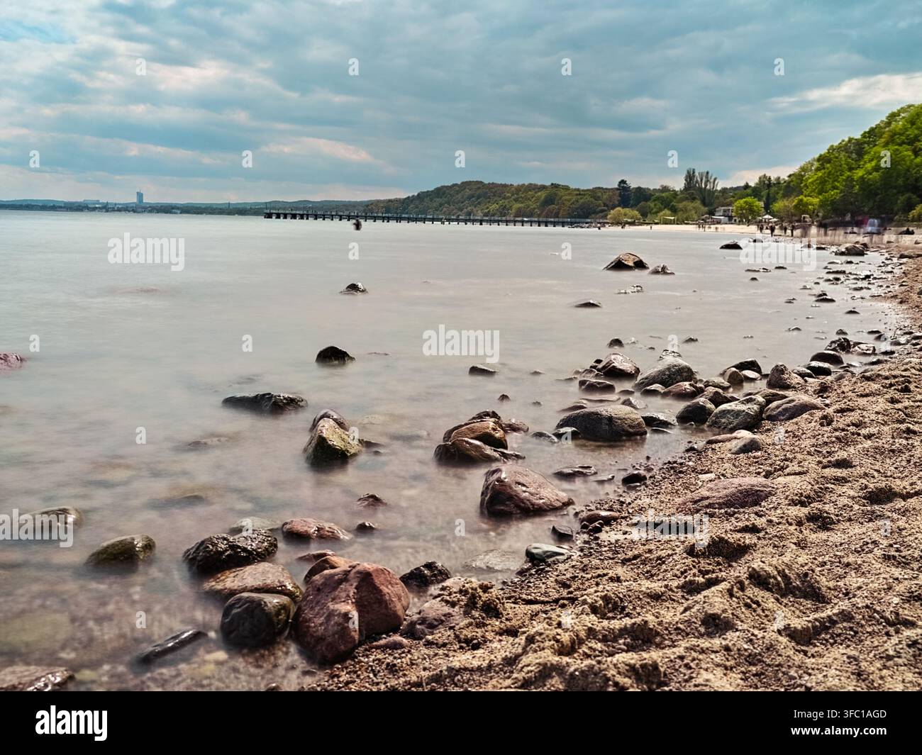 Fotografia a lunga esposizione della costa di Gdynia in Polonia, che mostra un mare tranquillo con acqua levigata, rocce sparse in primo piano e un d Foto Stock
