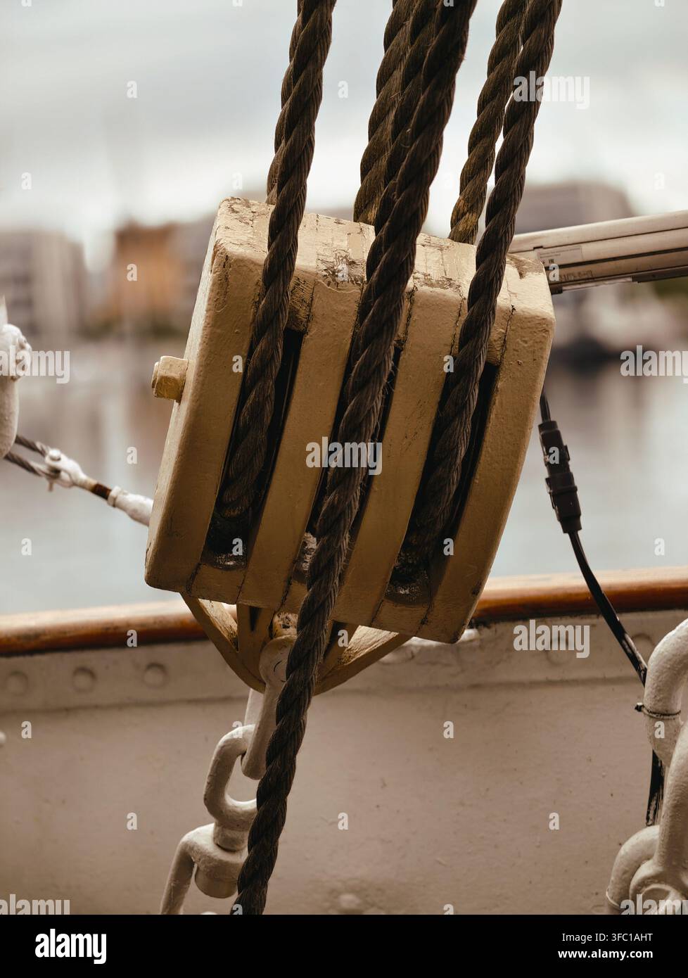 Un primo piano dettagliato di un sistema di pulegge in legno invecchiato con robuste funi su una nave a Gdynia, Polonia. La luce naturale evidenzia la trama Foto Stock