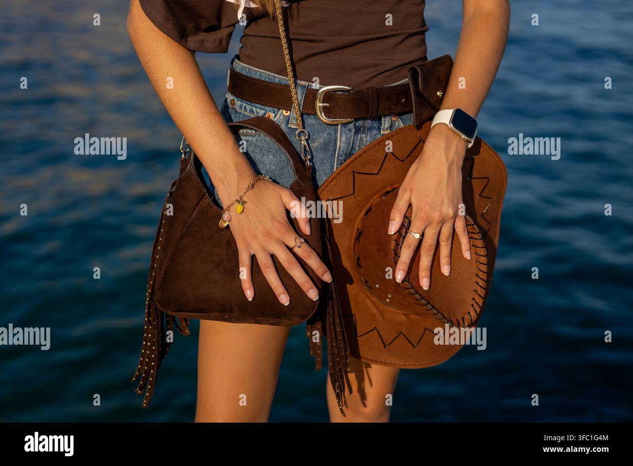 Moda western con cappello da cowboy in camoscio e borsa con frange. Primo piano di moda ispirata al western con pantaloncini di jeans, cappello da cowboy in camoscio, borsa con frange Foto Stock