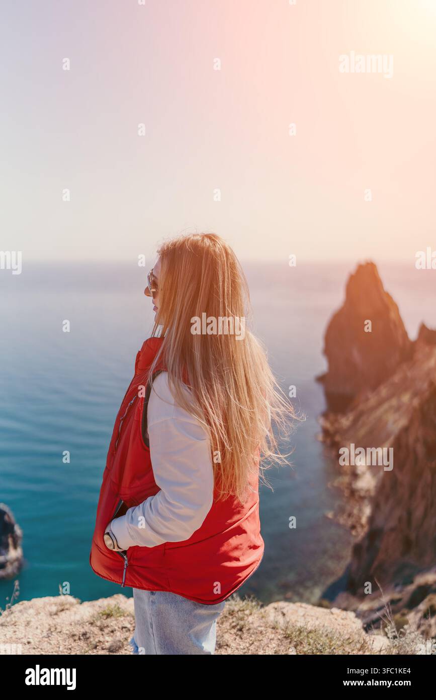 Donna in piedi su una scogliera sul mare, su un promontorio roccioso che guarda l'oceano blu sotto un cielo soleggiato, con spazio libero Foto Stock