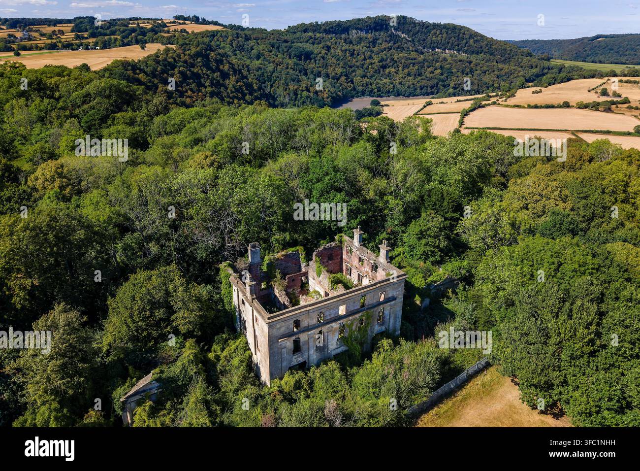 Villa georgiana abbandonata e in decadenza, circondata da alberi estivi, muri di mattoni e muratura sgretolati riconquistati dalla vegetazione sotto la luce chiara del giorno Foto Stock