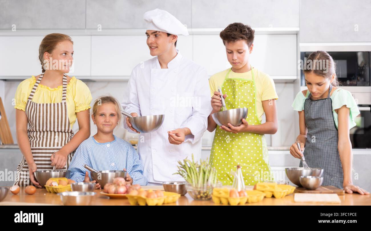 Giovane chef socievole che conduce corsi culinari a un gruppo di tween Foto Stock