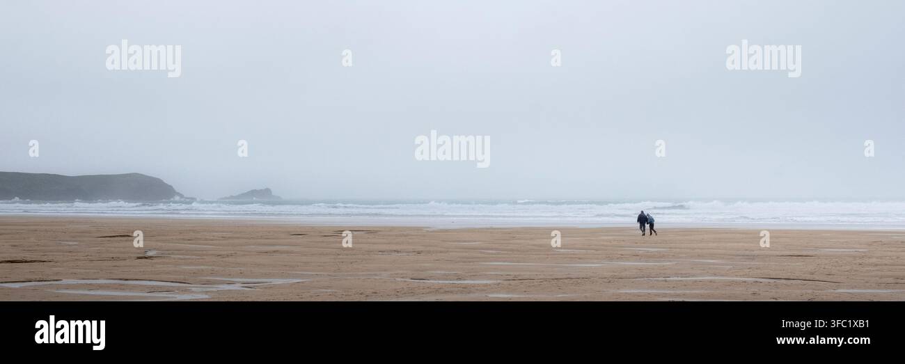 Un'immagine panoramica di una coppia che attraversa Fistral Beach in un clima nebbioso, afoso e freddo a Newquay in Cornovaglia nel Regno Unito. Foto Stock