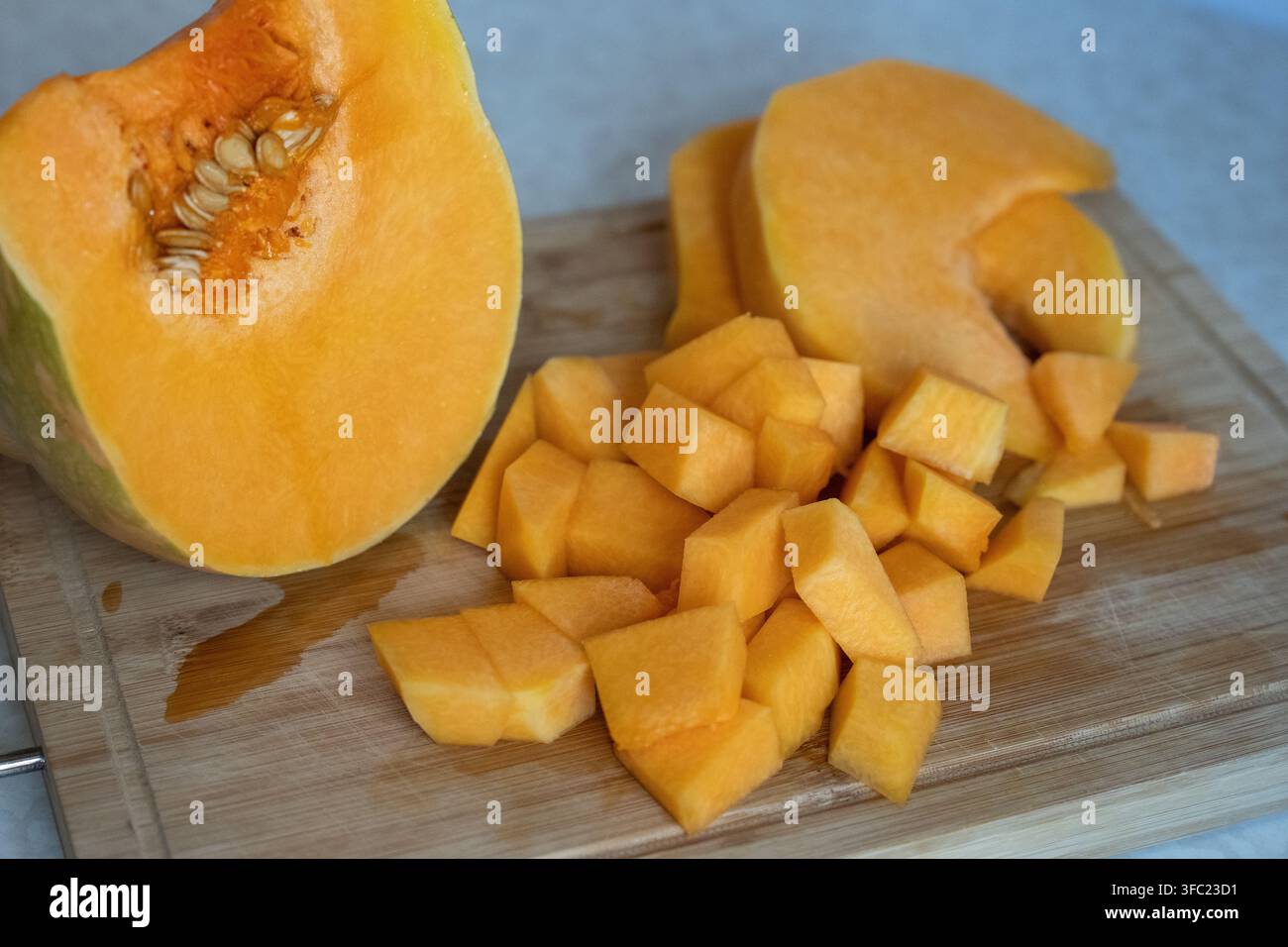 Zucca butternut fresca tagliata a cubetti e a spicchi su un tagliere di legno. Vista ravvicinata della preparazione del cibo con zucca d'inverno arancione, semi e fetta Foto Stock