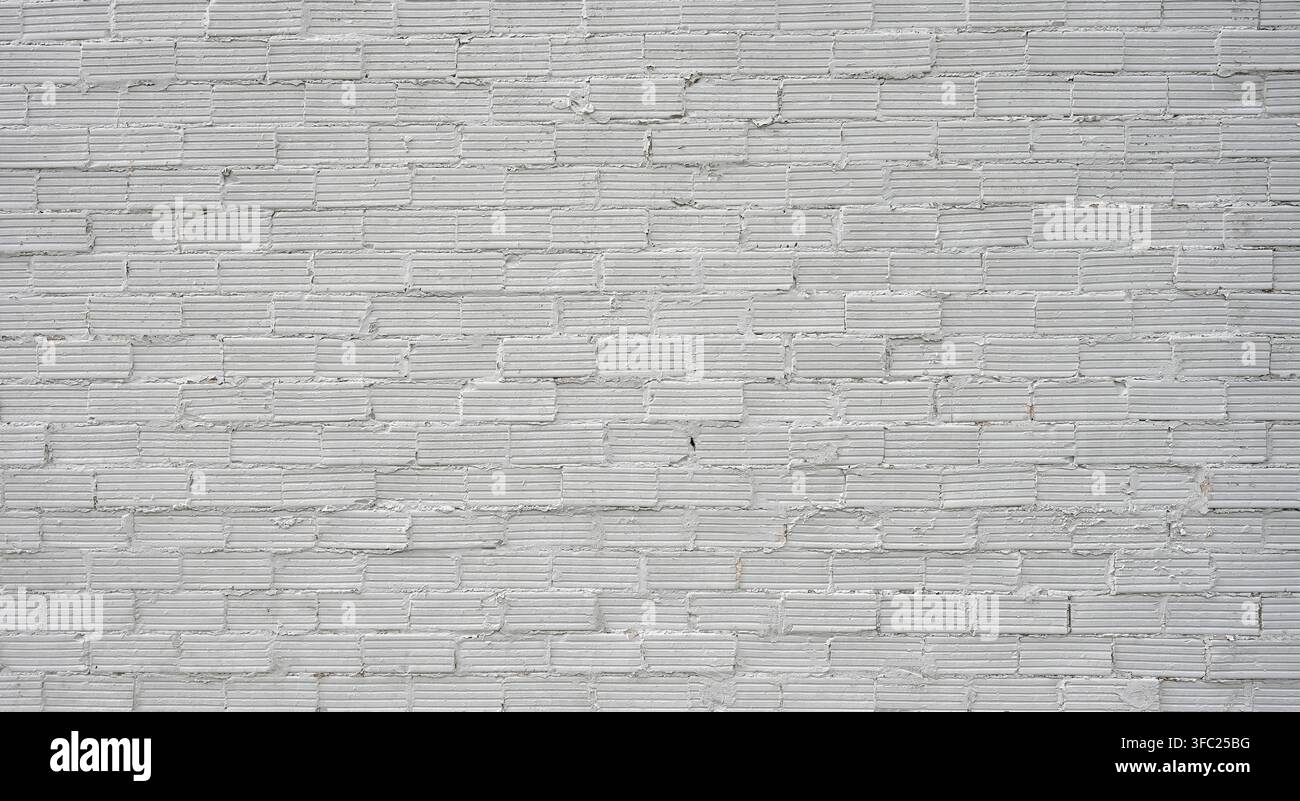 Superficie ruvida di muro in mattoni e malta dipinta di bianco con mattoni sporgenti irregolari e texture di mattoni scanalati uniforme Foto Stock