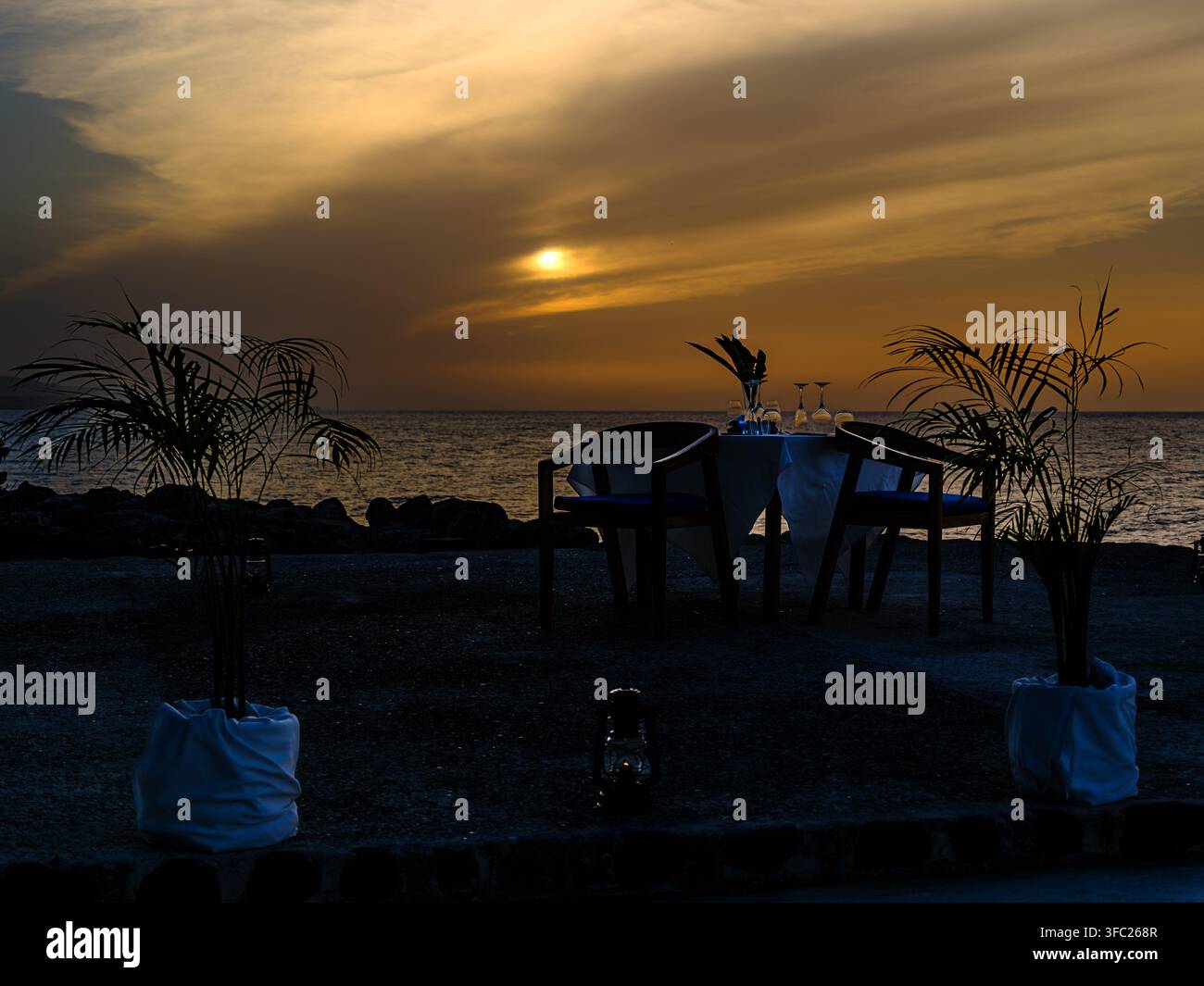 Tavolo da pranzo privato allestito al tramonto accanto al Mar dei Caraibi al resort GoldenEye, Oracabessa, Giamaica, con posate, lanterne e palme tropicali in silhouette Foto Stock