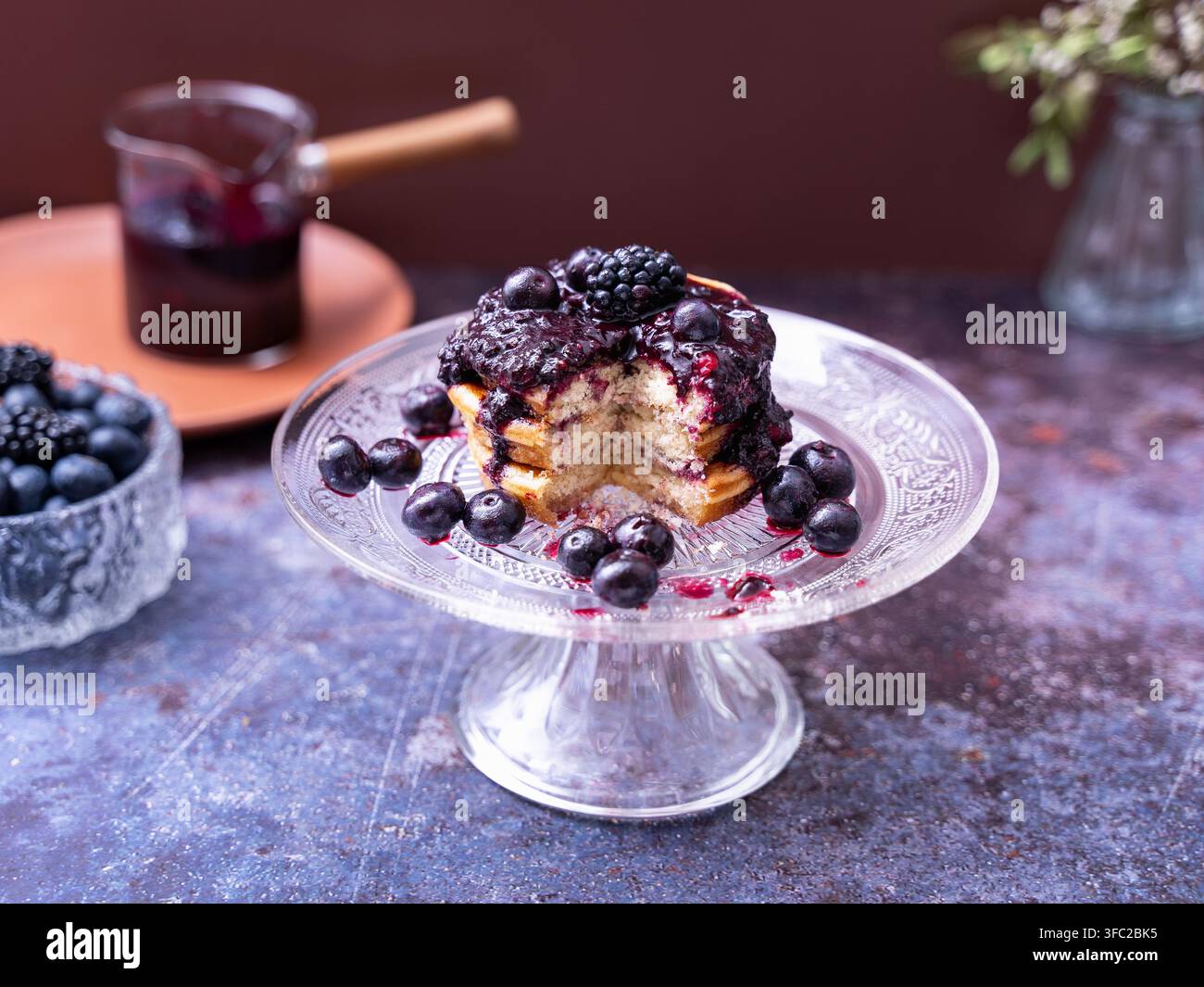 Pancake fatti in casa guarniti con composta di bacche e bacche fresche serviti su un elegante supporto per torta in vetro Foto Stock