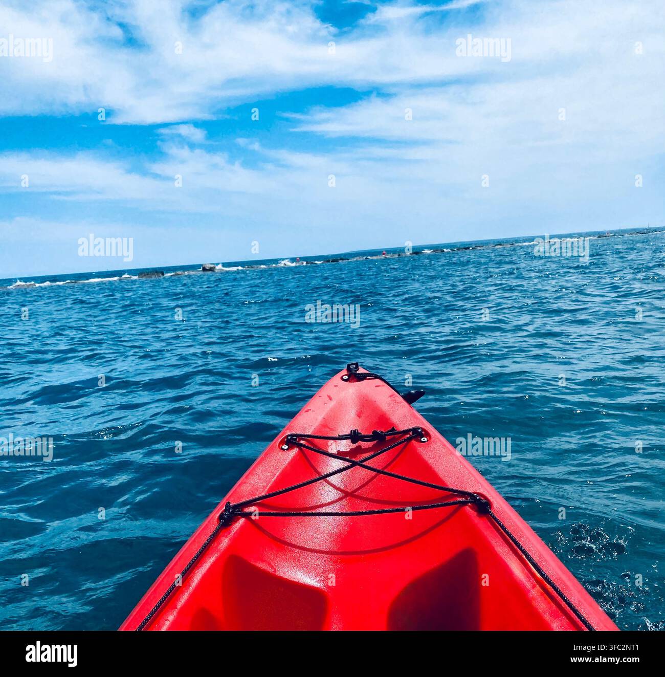 La prua di un kayak rosso si sposta sull'acqua blu aperta verso un orizzonte roccioso basso sotto nuvole morbide. - Immagine stock catturata con smartphone