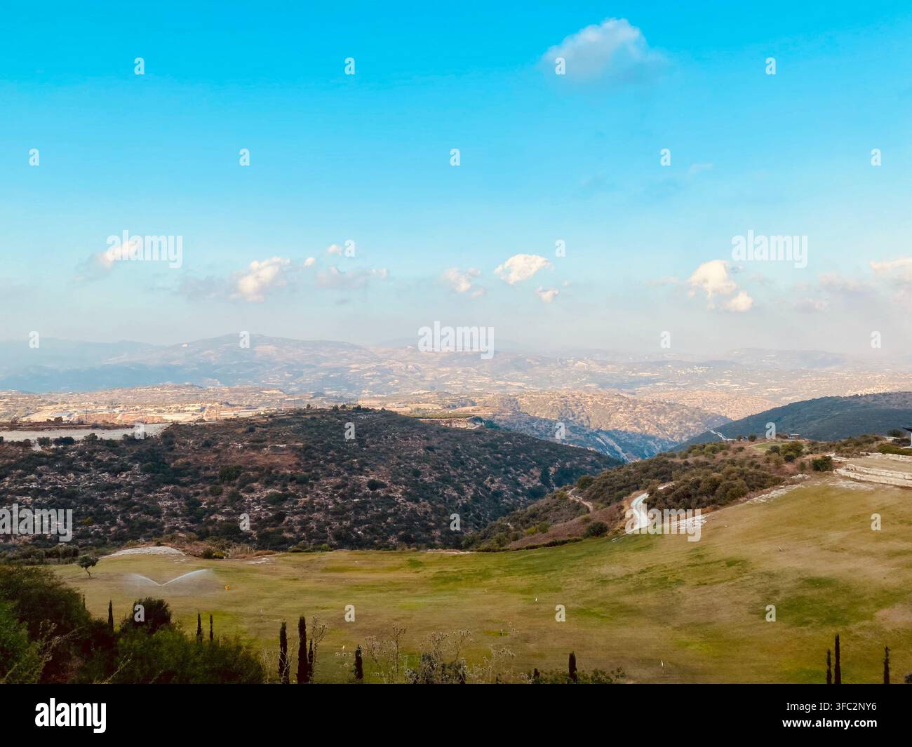 Colline verdi ondulate e una vasta valle montana si estendono sotto nuvole morbide e un cielo blu terso. - Immagine stock catturata con smartphone
