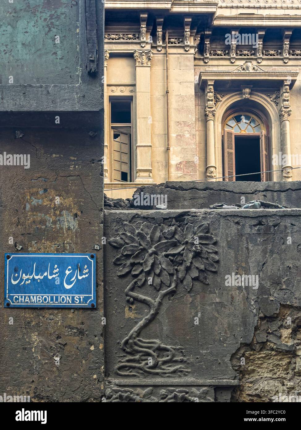Egitto, Il Cairo, centro città, un cartello stradale per Rue Champollion, con il Palazzo di Said Halim Pasha – noto anche come Palazzo Champollion – che cade in rovina sullo sfondo a causa della mancanza di lavori di restauro Foto Stock