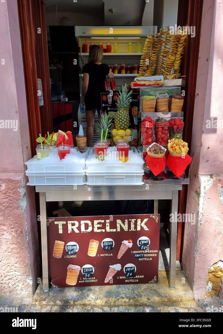 Praga, Repubblica Ceca – 28 luglio 2026: Una bancarella di street food espone dolci trdelnik, snack di patate a spirale, frutta fresca e bevande fredde. Foto Stock