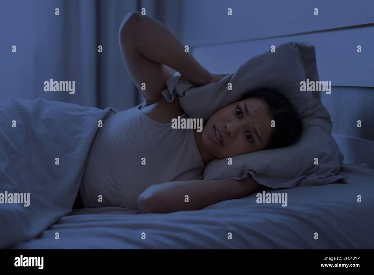 Giovane donna nera sdraiata sveglia di notte con un cuscino sull'orecchio Foto Stock
