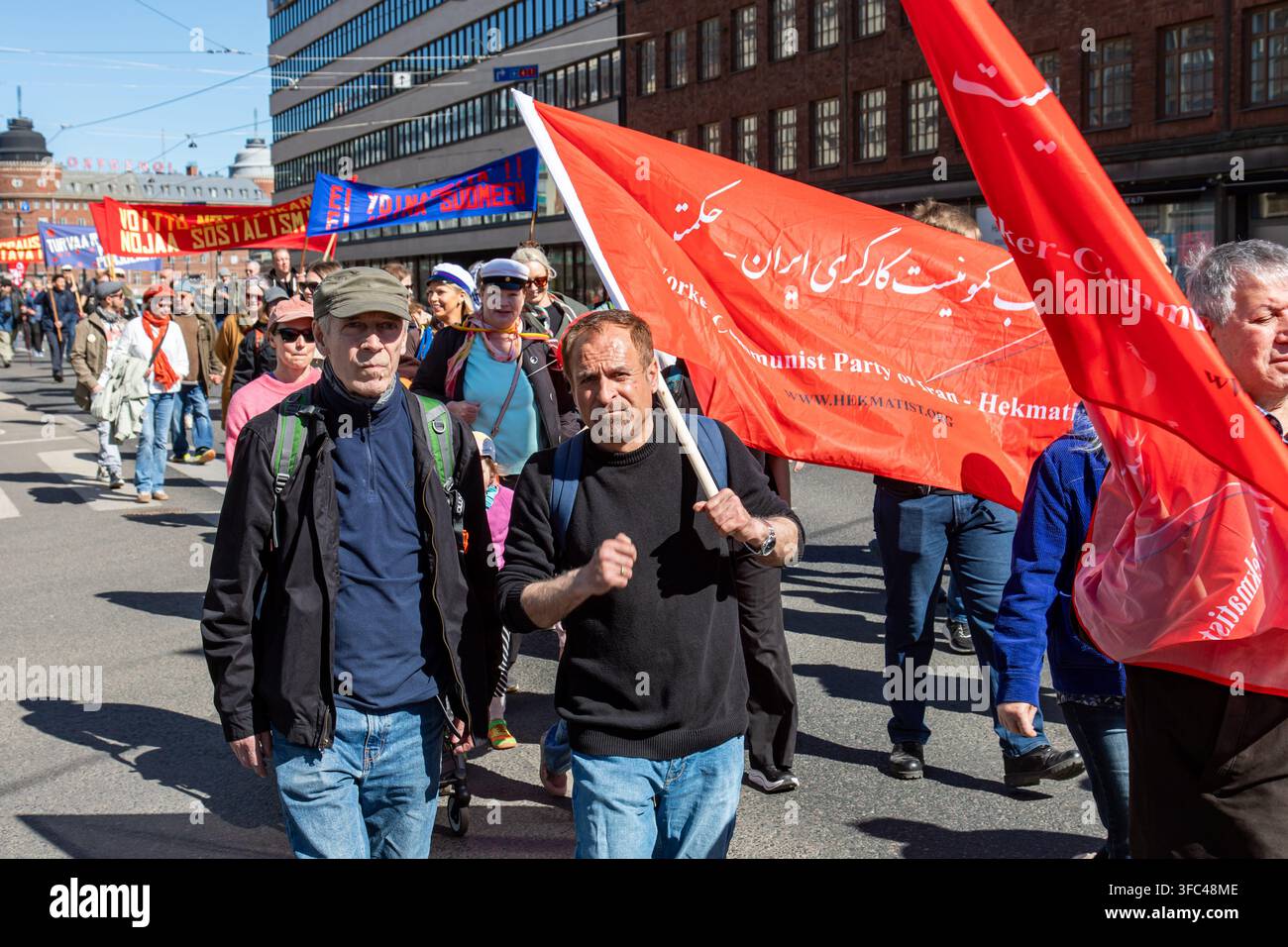 Uomini che portano bandiere del Partito Comunista Operaio dell'Iran in una manifestazione del Primo Maggio nel quartiere di Hakaniemi a Helsinki, Finlandia Foto Stock