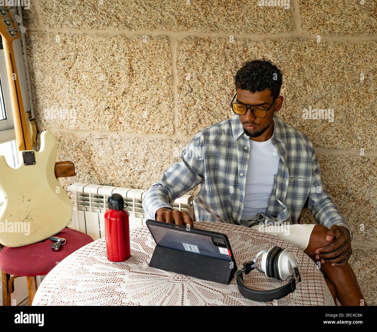 Giovane uomo concentrato che usa un tablet a un tavolo accanto a una chitarra Foto Stock