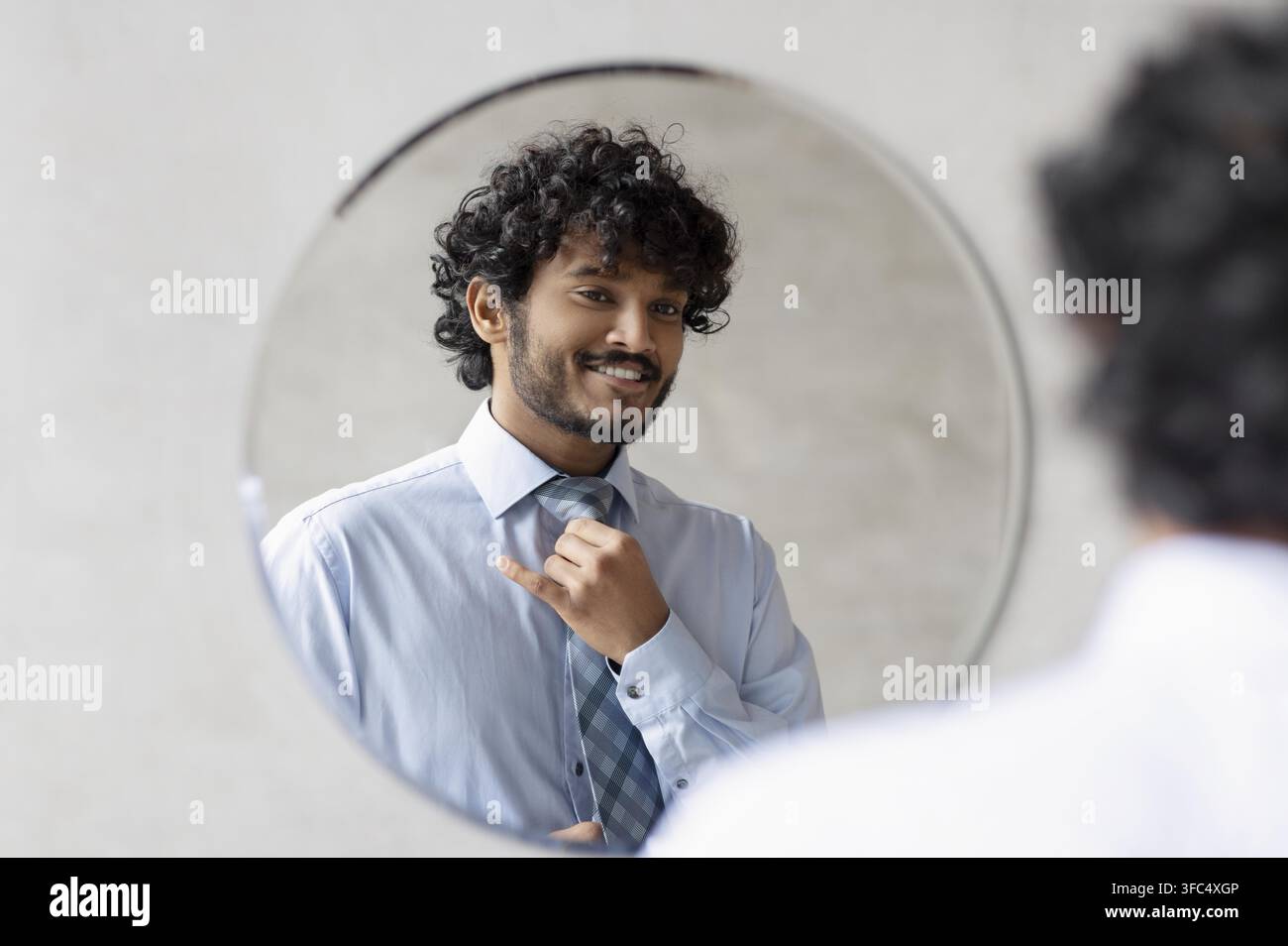 Giovane uomo sorridente che aggiusta la cravatta davanti allo specchio, concetto aziendale Foto Stock