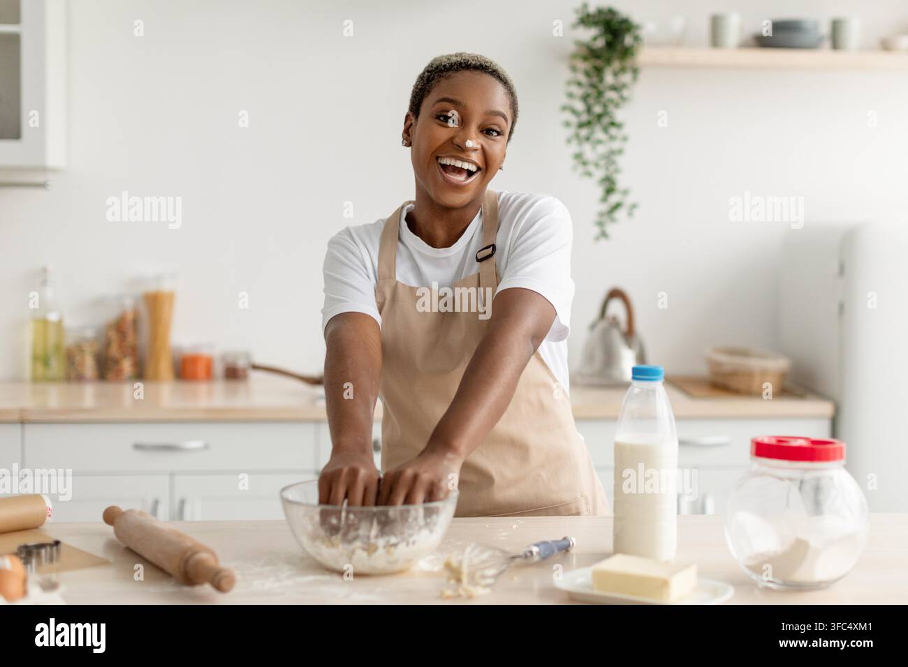 Chef donna nera sorridente che mescola l'impasto al bancone della cucina, concetto di cucina Foto Stock