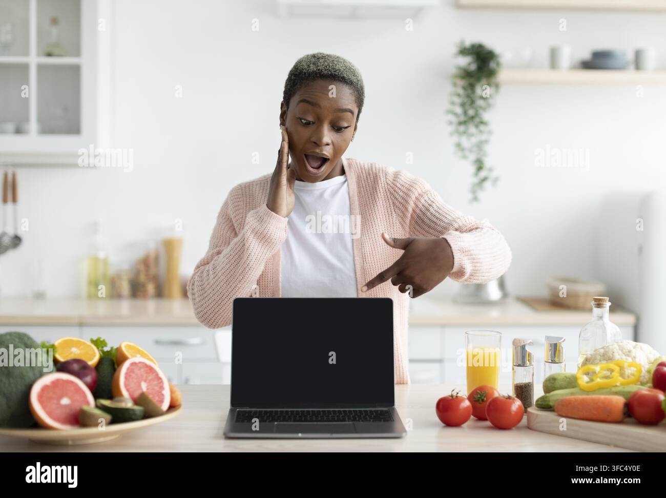 Donna nera entusiasta che indica lo schermo del laptop in una cucina moderna, concetto di vita sana Foto Stock