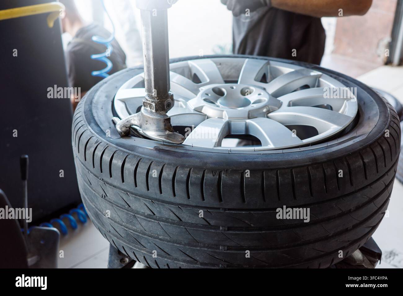 Servizio di montaggio pneumatici con meccanico che monta la gomma su cerchio in lega utilizzando un cambiapneumatici, manutenzione dell'officina automobilistica per la sostituzione, la riparazione delle ruote e una guida sicura. Foto Stock