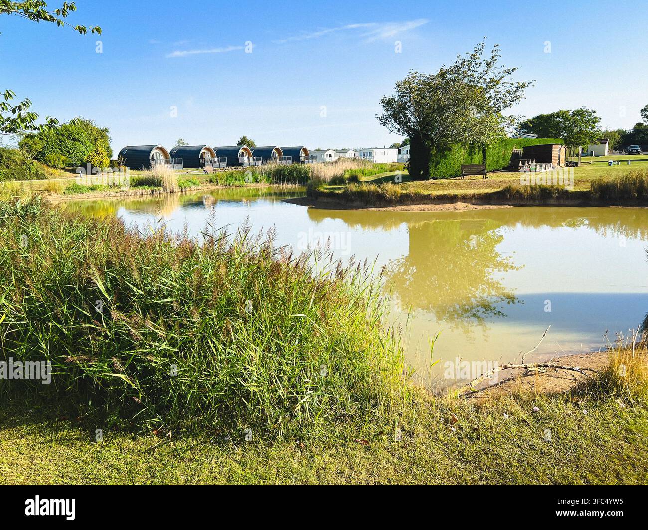 Uno stagno in un parco vacanze, una scena rilassante con pod di campeggio sullo sfondo - Immagine stock catturata con smartphone