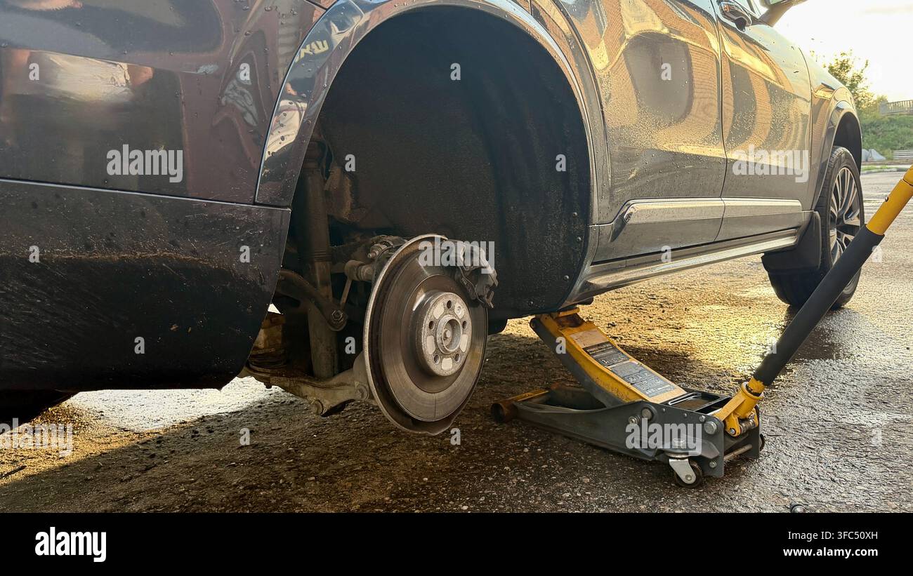 Prima di un'automobile passeggera con la ruota rimossa durante la sostituzione degli pneumatici. Foto Stock