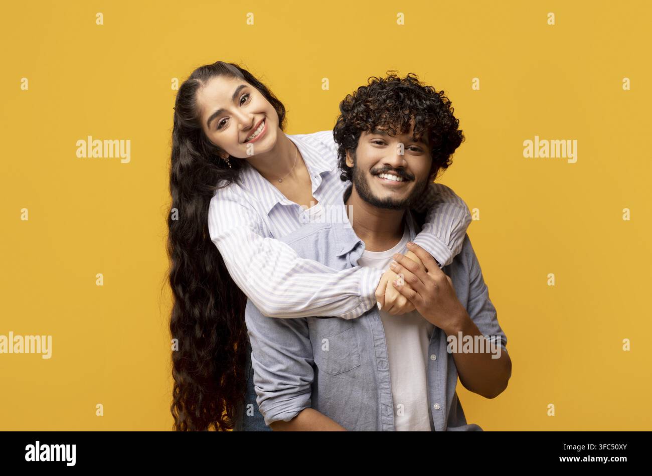 Coppia felice di razza mista che si abbraccia con volti sorridenti, sfondo giallo Foto Stock