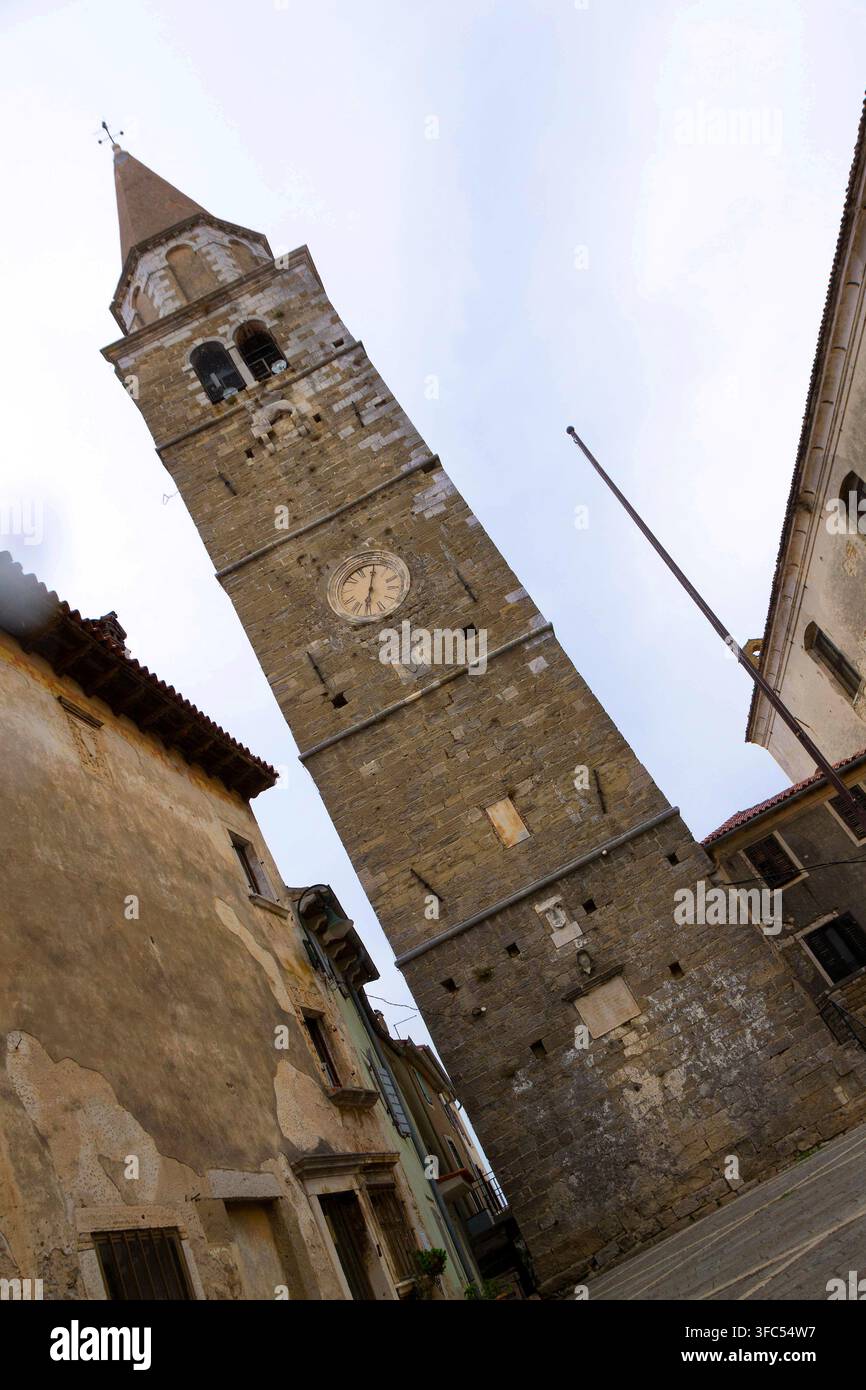 Prospettiva a basso angolo che guarda verso l'alto verso il torre campanaria storica in pietra della Chiesa di San Servulo con un grande orologio, situata nella piazza medievale di Bu Foto Stock