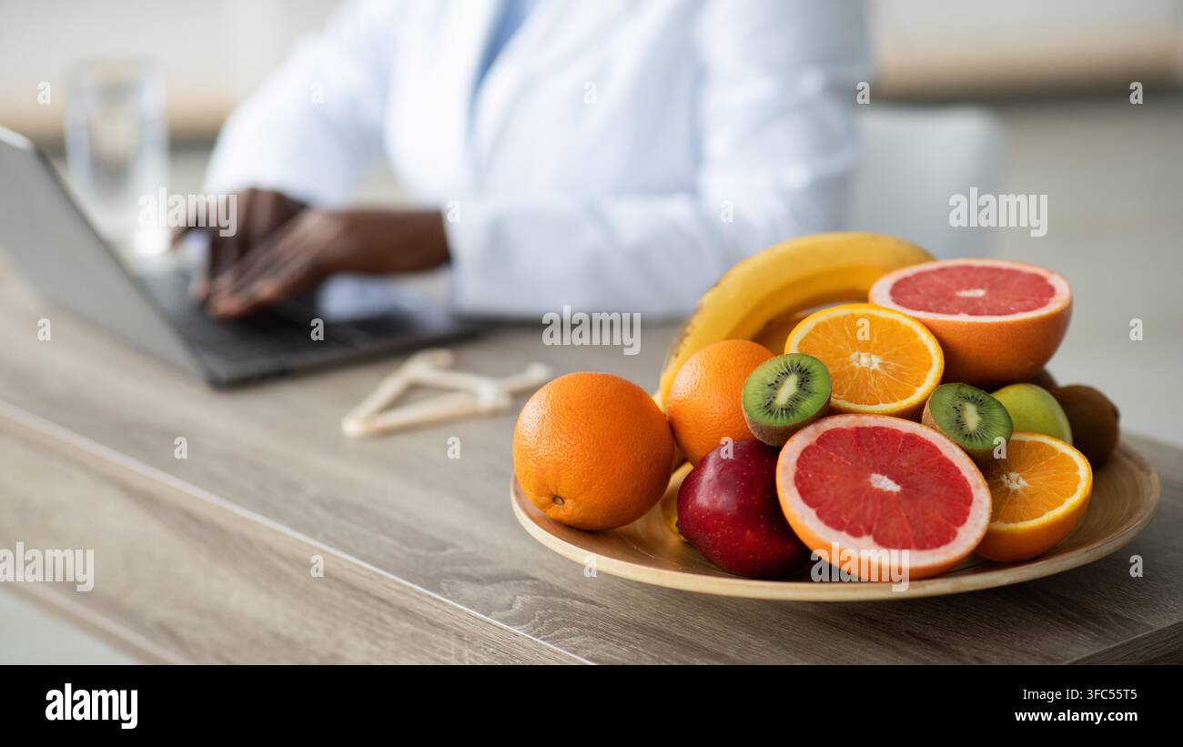 Nutrizionista che lavora su un laptop con frutti sani in clinica, concetto di perdita di peso Foto Stock