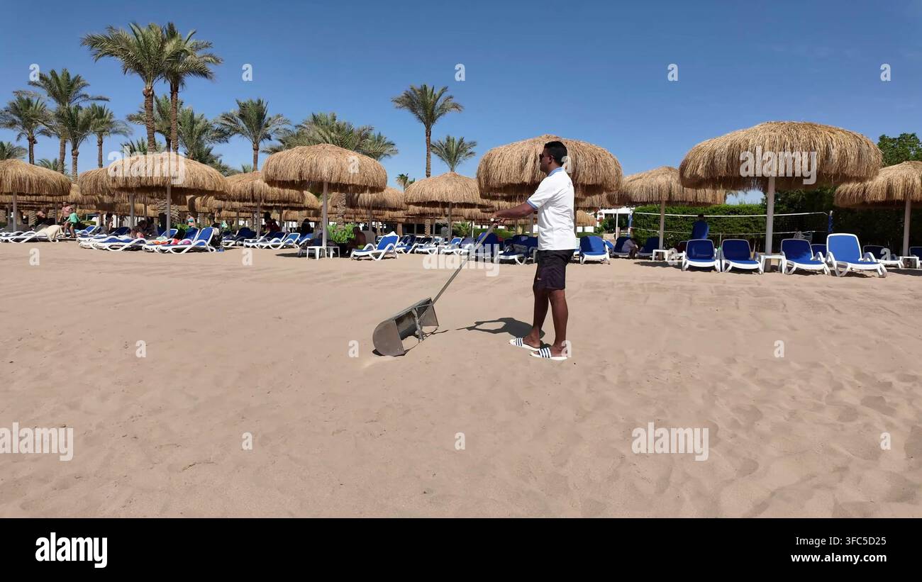 SHARM EL SHEIKH, EGITTO – 10 GIUGNO 2026: Un membro del personale che pulisce la sabbia della spiaggia con un rastrello in un resort a Sharm el Sheikh. Foto Stock