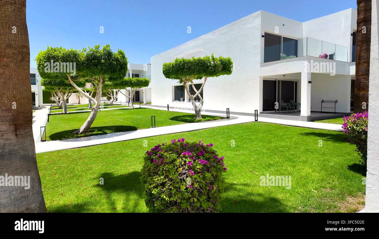 SHARM EL SHEIKH, EGITTO - 10 GIUGNO 2026: Prato verde ben curato con alberi potati e edifici bianchi di un resort di lusso a Sharm el Sheikh. Foto Stock