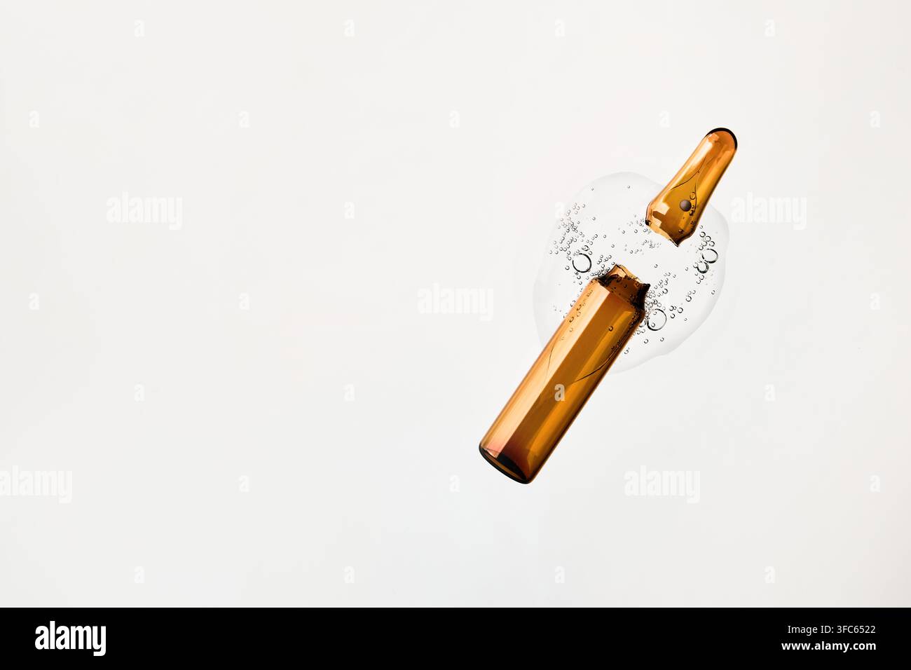 Ampolla di vetro rotta che riversa siero cosmetico con bolle d'aria su sfondo bianco Foto Stock