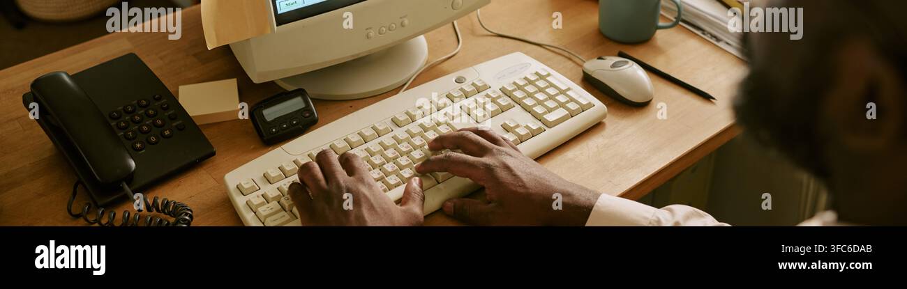 Intestazione delle mani di un uomo nero che digita su una tastiera di computer retrò in un ufficio vintage Foto Stock