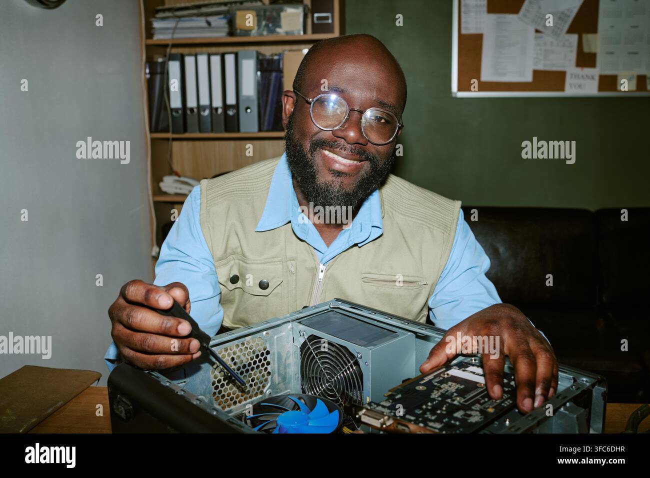 Ritratto di un uomo nero sorridente che ripara un computer in un ufficio retrò Foto Stock