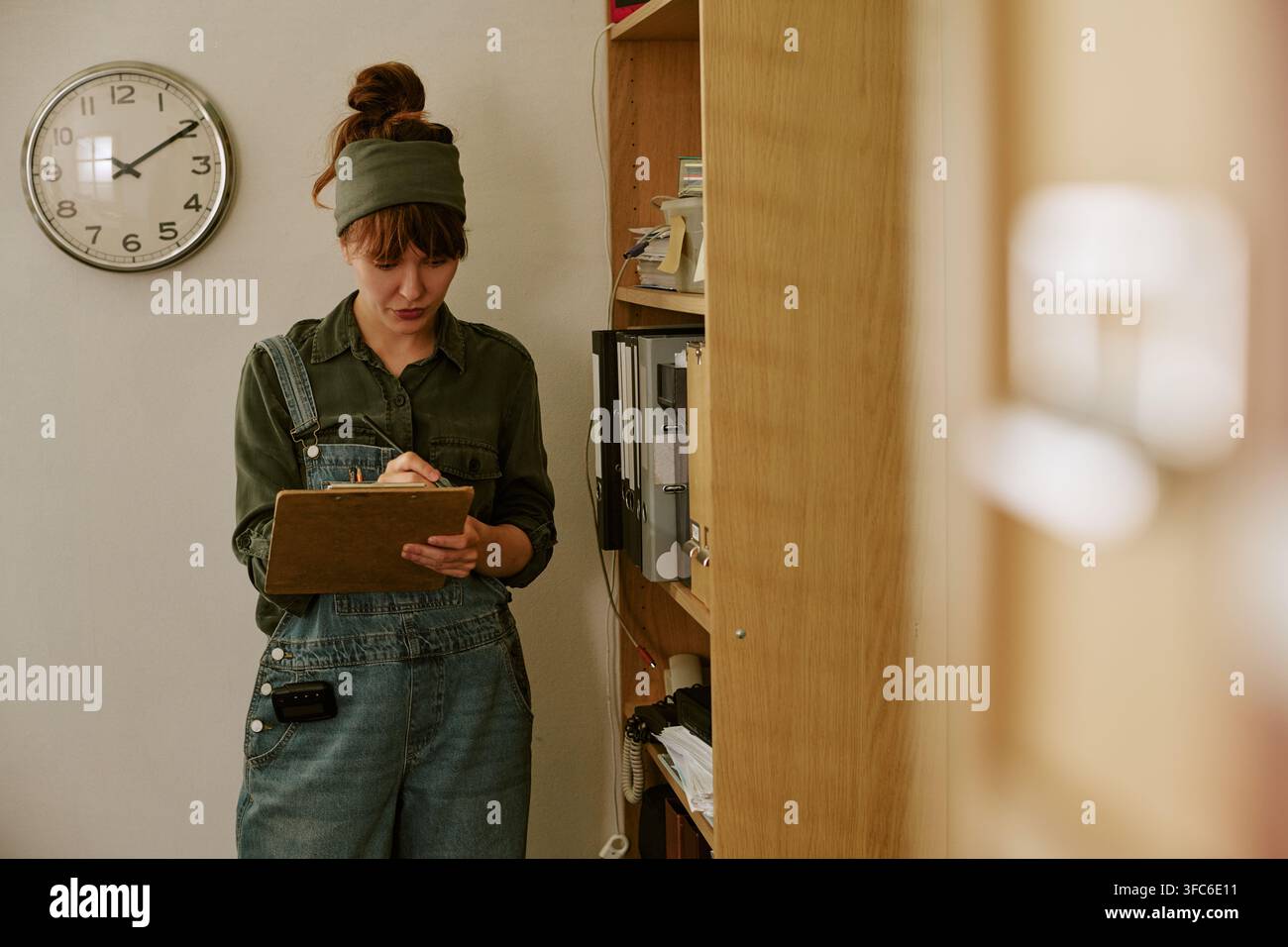 Donna che scrive su una clipboard in un ufficio retrò e lavora come archivista Foto Stock