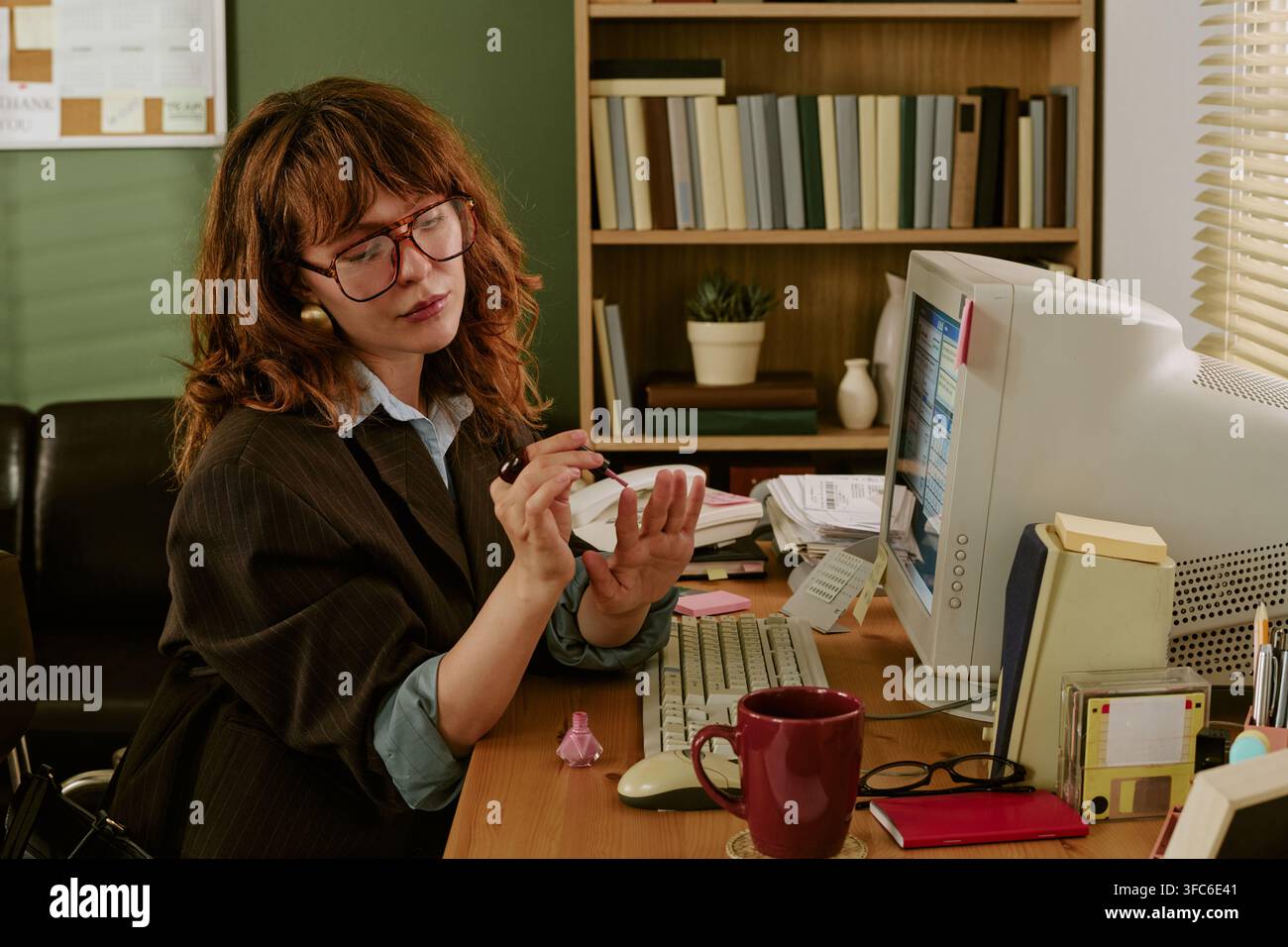 Dipendente d'ufficio che si dipinge le unghie a una scrivania da lavoro retrò Foto Stock