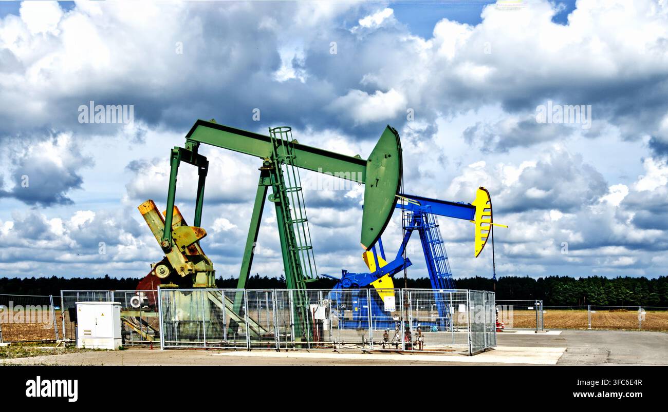 Pompe oleose che lavorano per estrarre petrolio greggio dal suolo sotto un cielo nuvoloso, rappresentando l'industria dei combustibili fossili Foto Stock