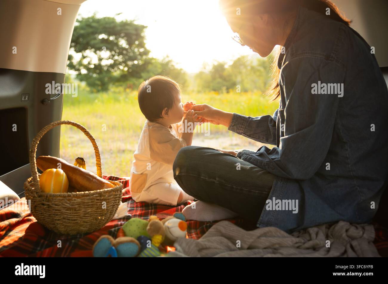 Madre che nutre il suo bambino con una banana e uno spuntino sano durante il campeggio in auto Foto Stock