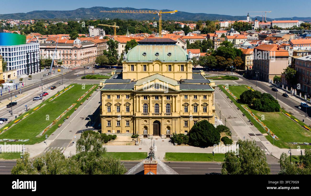 Vista aerea del Teatro Nazionale Croato con la sua distintiva facciata gialla e il tetto verde, circondato da parchi urbani e dal paesaggio cittadino di Zagr Foto Stock