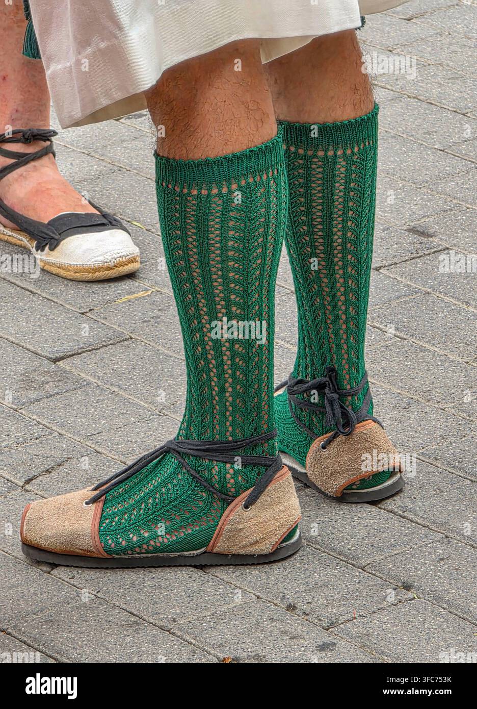 Il partecipante è in piedi su una superficie di pietra. Le sue gambe sono visibili, mostrando calzini verde brillante fino al ginocchio con un motivo a maglia. Indossa espadrilles marrone con Foto Stock