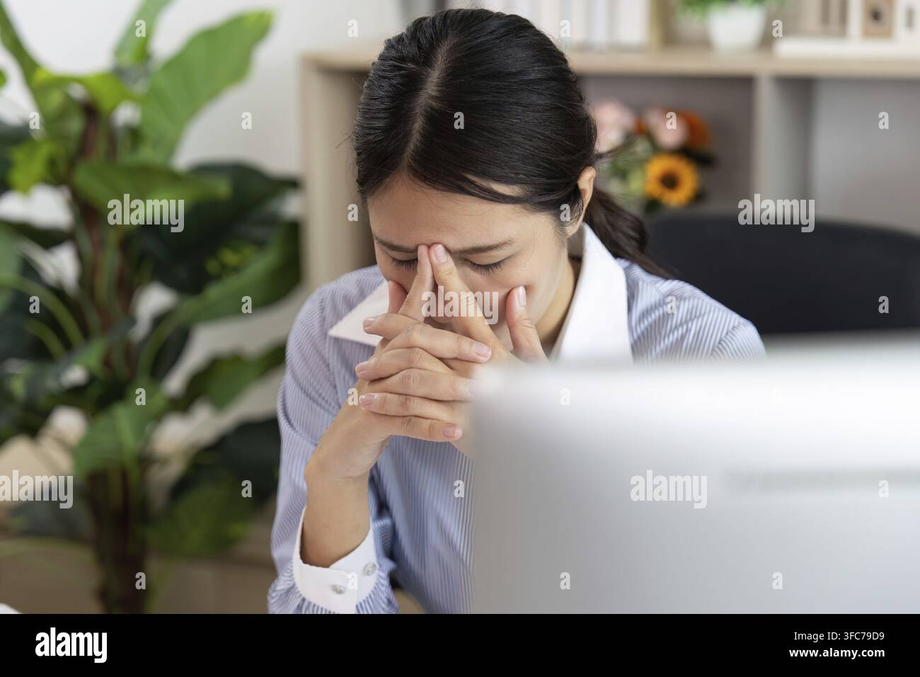 Una donna disperata alla sua scrivania che tiene il viso per frustrazione e mostra l'impatto emotivo della sindrome da ufficio Foto Stock