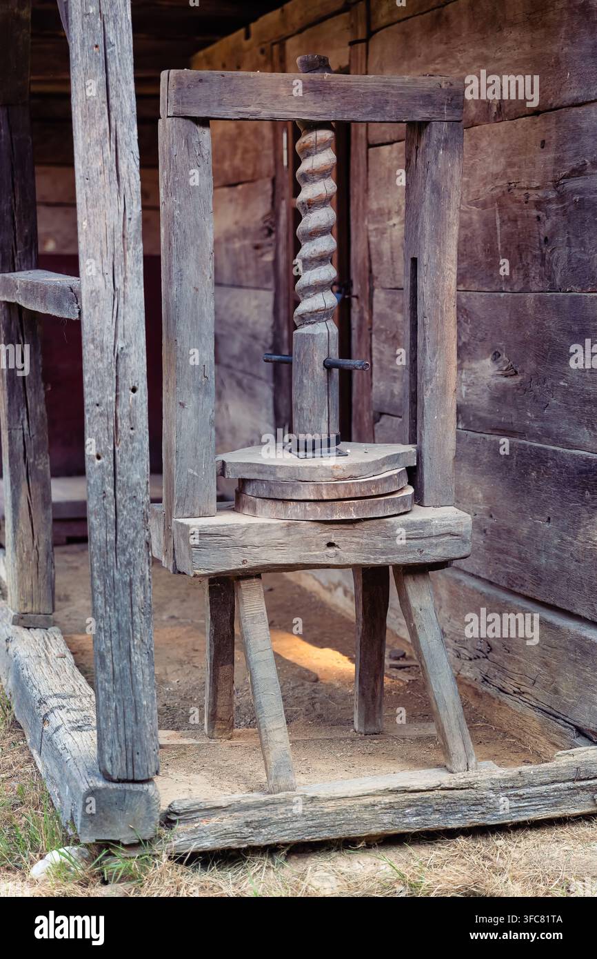 Vecchia pressa a vite in legno accanto a un muro di casa in legno rustico in un contesto rurale tradizionale in Romania Foto Stock