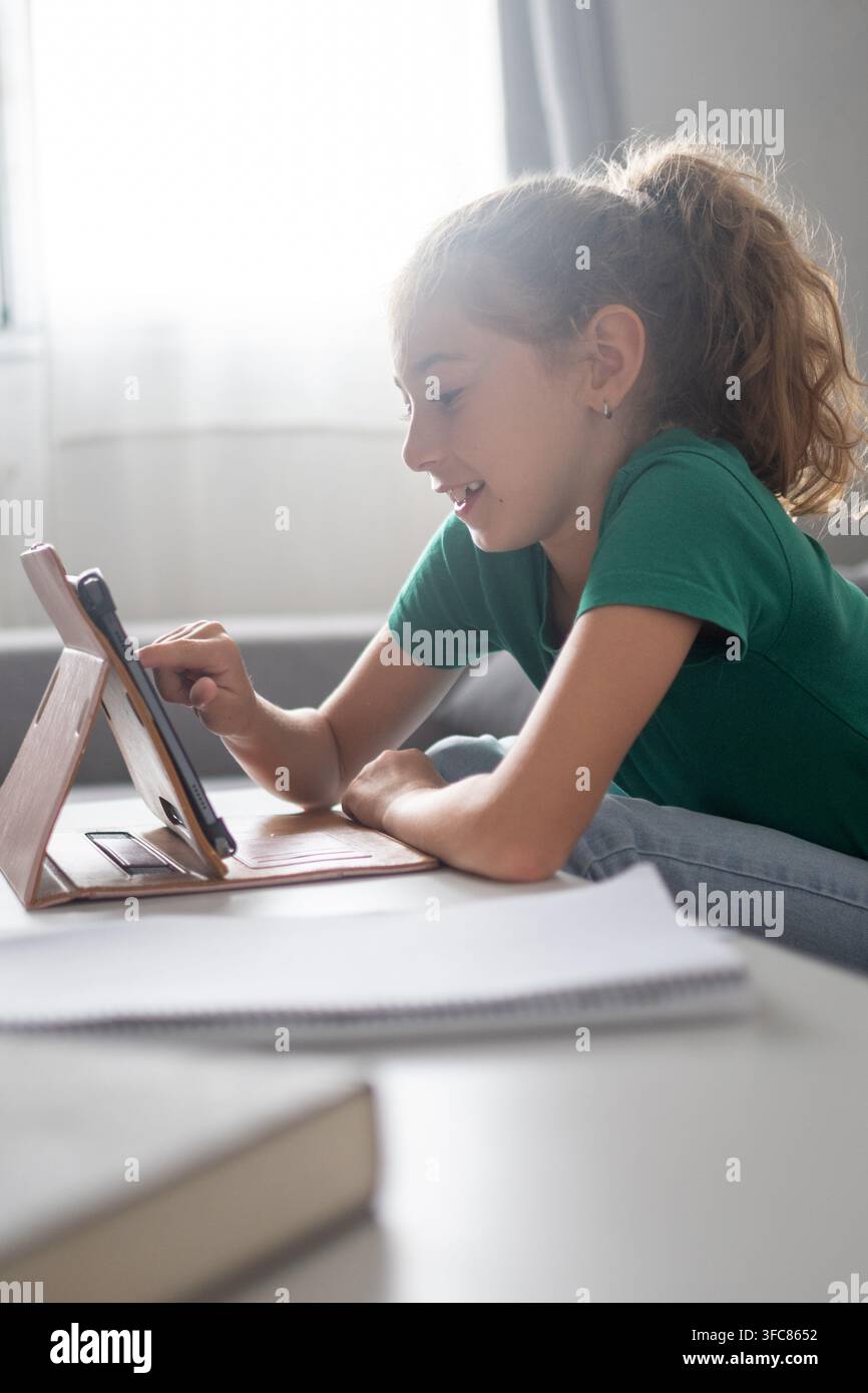 Studentessa che utilizza un tablet a casa mentre studia con quaderni e materiale didattico durante il tempo dei compiti. Foto Stock