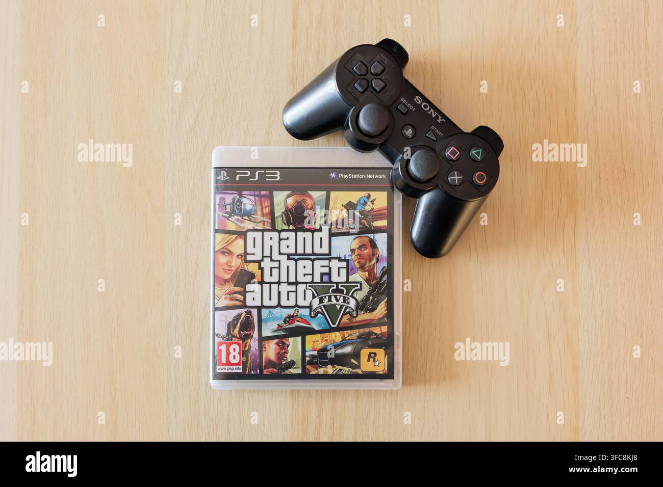 Gioco GTA V con un controller Playstation. Grand Theft Auto 5 di Rockstar Games appoggiato su un tavolo. Primo piano della copertina del videogioco nella custodia. Foto Stock