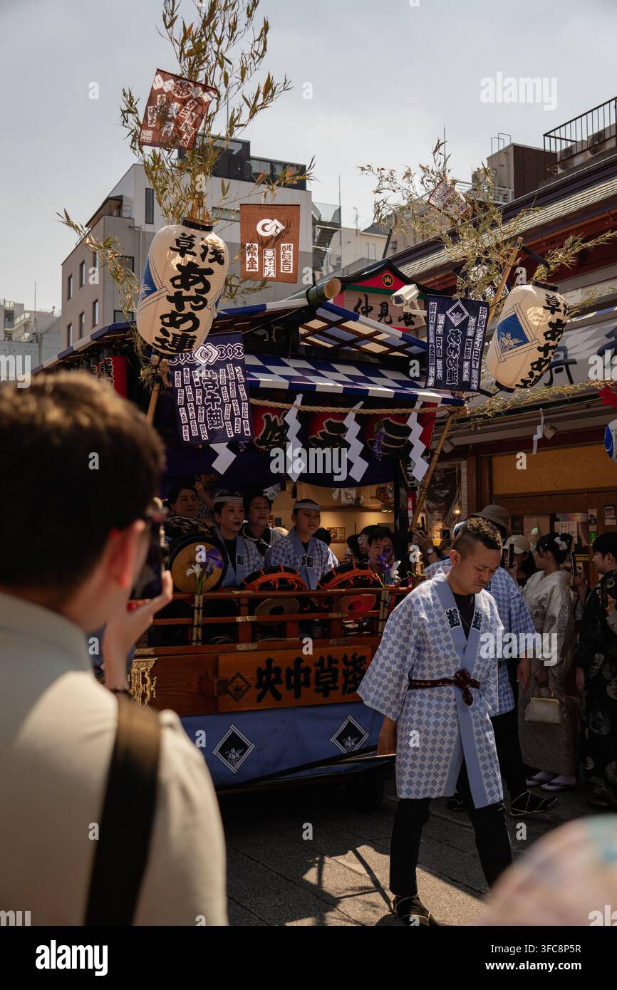 Taito City, Giappone - 15 maggio 2026: Vista della carrozza del festival di Asakusa con musicisti in tradizionali mantelli happi e lanterne di carta sotto un cielo sereno. Foto Stock