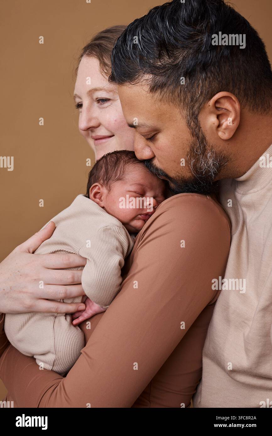 Genitori multirazziali che abbracciano un neonato in un tenero ritratto di famiglia che mostra amore e legame Foto Stock