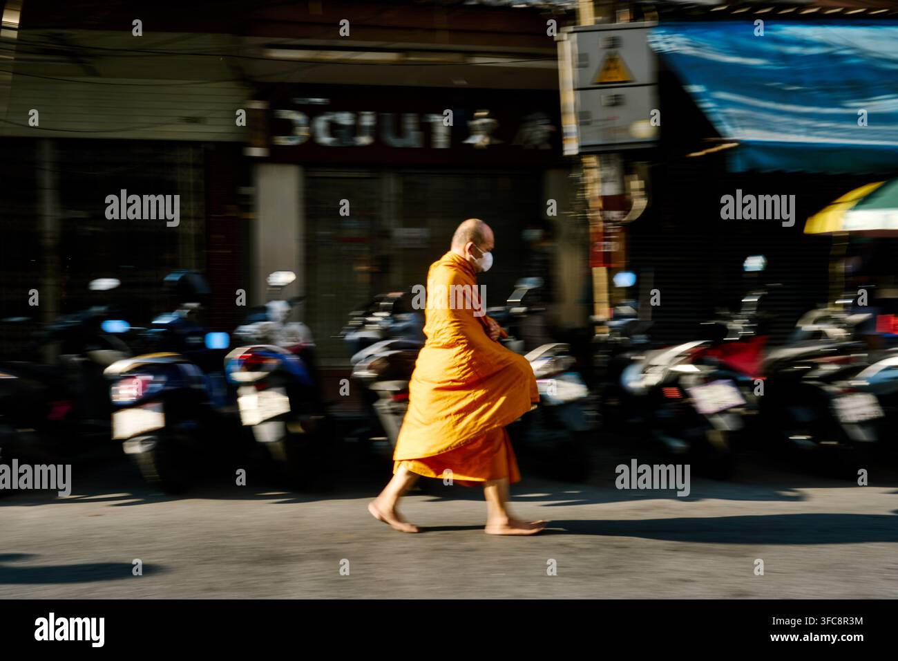 Monaco buddista che cammina lungo Thanon Si Wiang a Bangkok, Thailandia, catturato con una velocità di otturatore lenta che crea sfocatura del movimento. Foto Stock