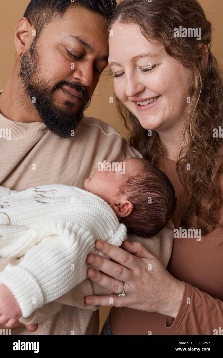 Genitori multirazziali teneri che tengono un neonato in un ritratto familiare caldo, abbracciando la genitorialità e l'amore Foto Stock