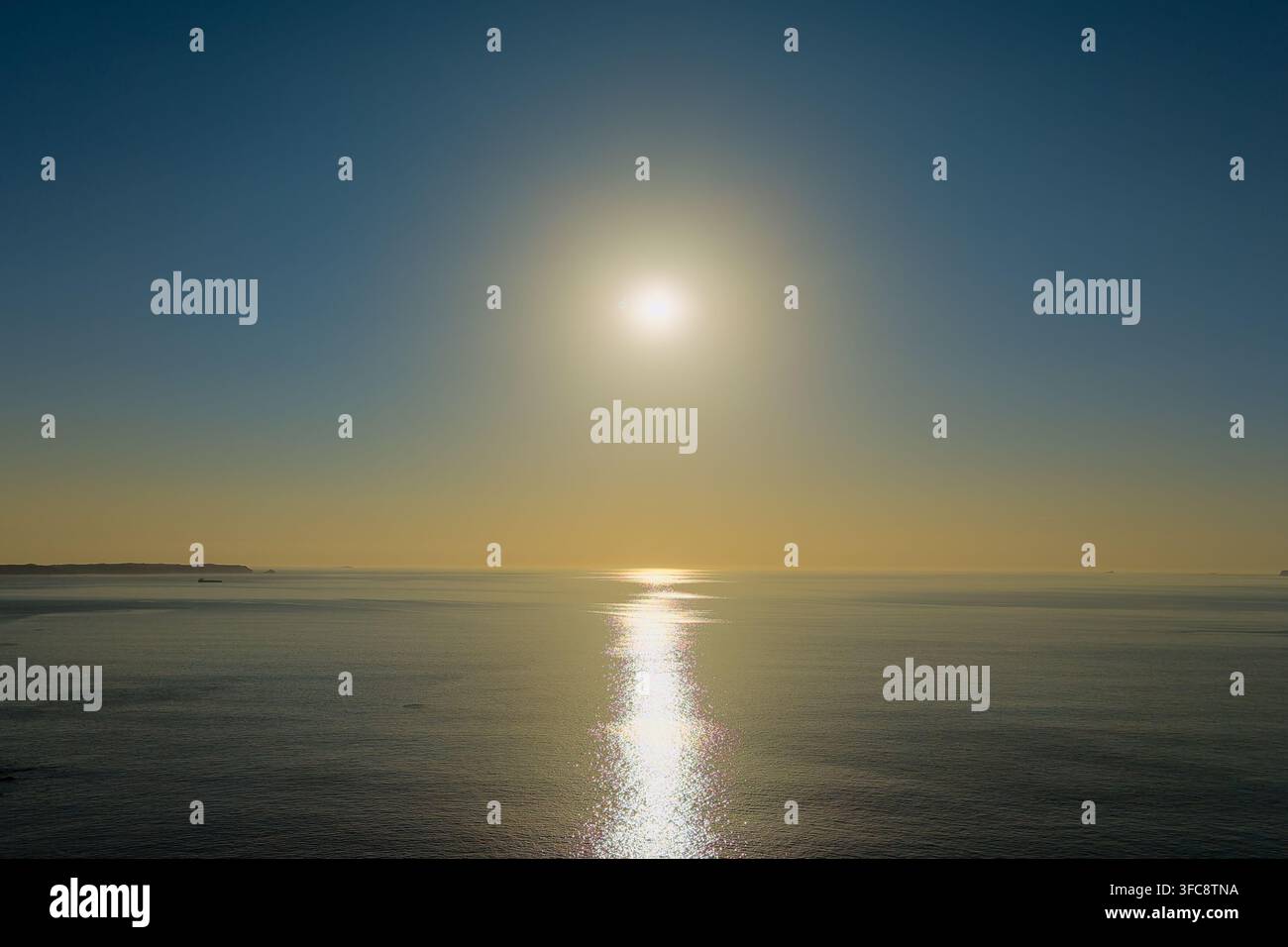 Sole luminoso che splende sulle acque calme del Mare d'Irlanda lungo la costa del Pembrokeshire nel Galles, cielo sereno e riflesso di un raggio dorato del sole sulla superficie dell'acqua al tramonto Foto Stock